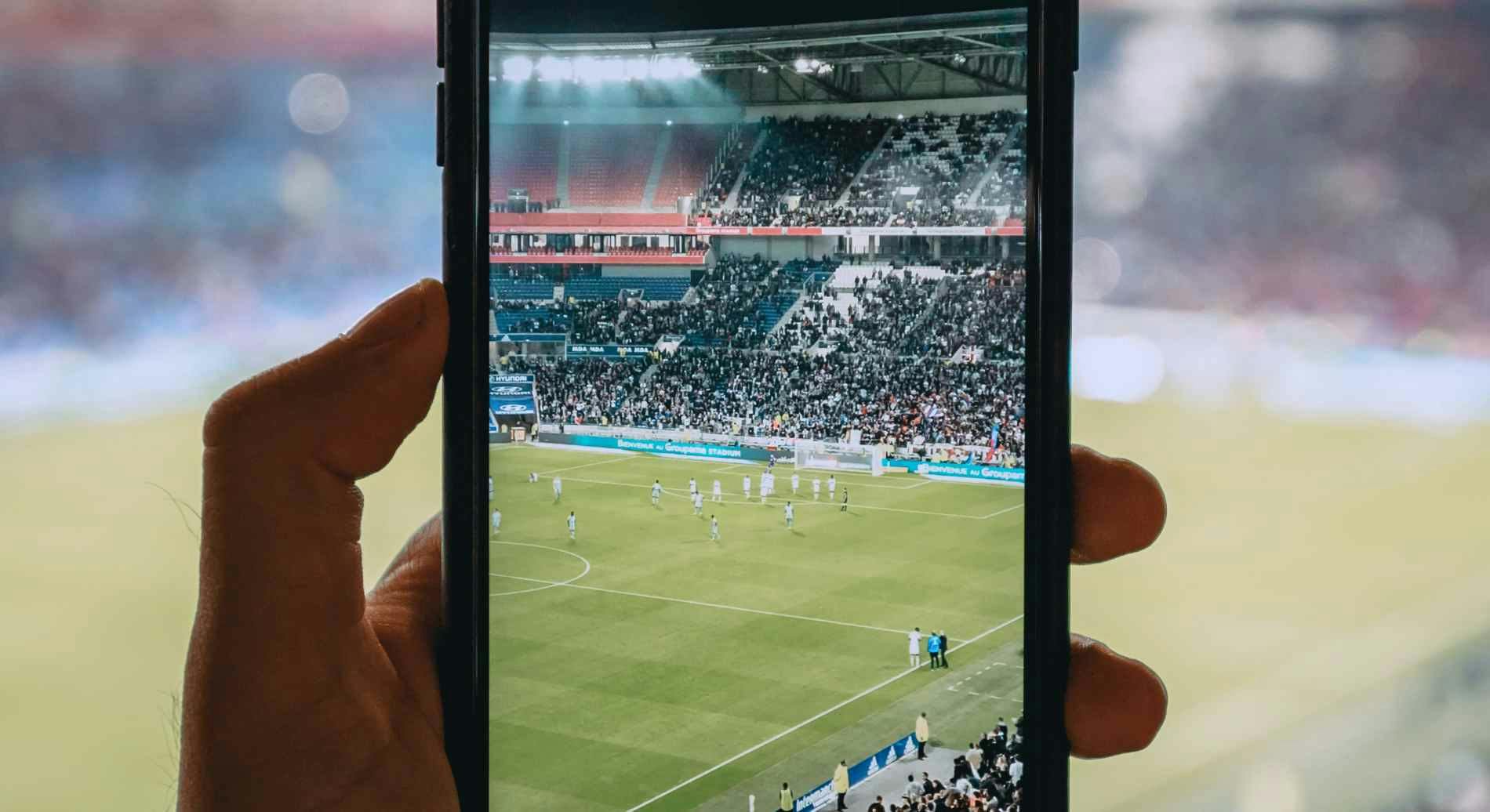 Imagem de uma pessoa filmando um estádio em um jogo de futebol