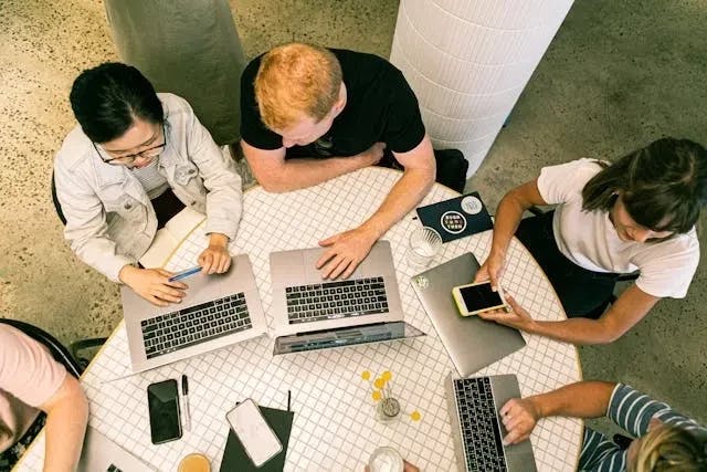 time de marketing com 3 pessoas reunidas em uma mesa mexendo em seus notebooks