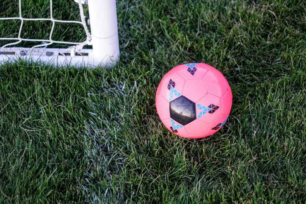 Imagem de uma bola de futebol nos tons rosa e preto em cima de um campo, também de futebol