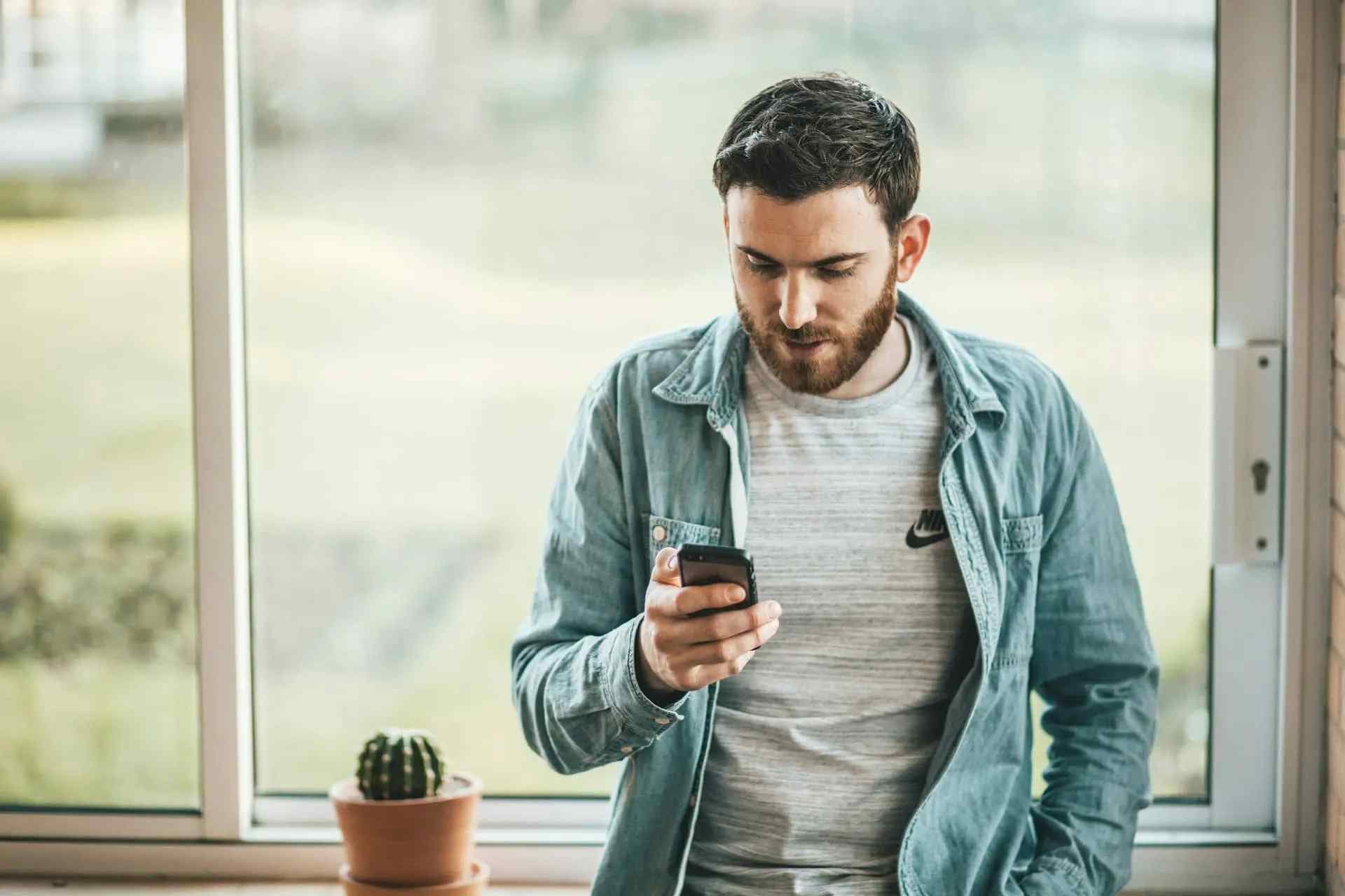 Imagem de um homem usando um celular, escorado em uma janela fechada