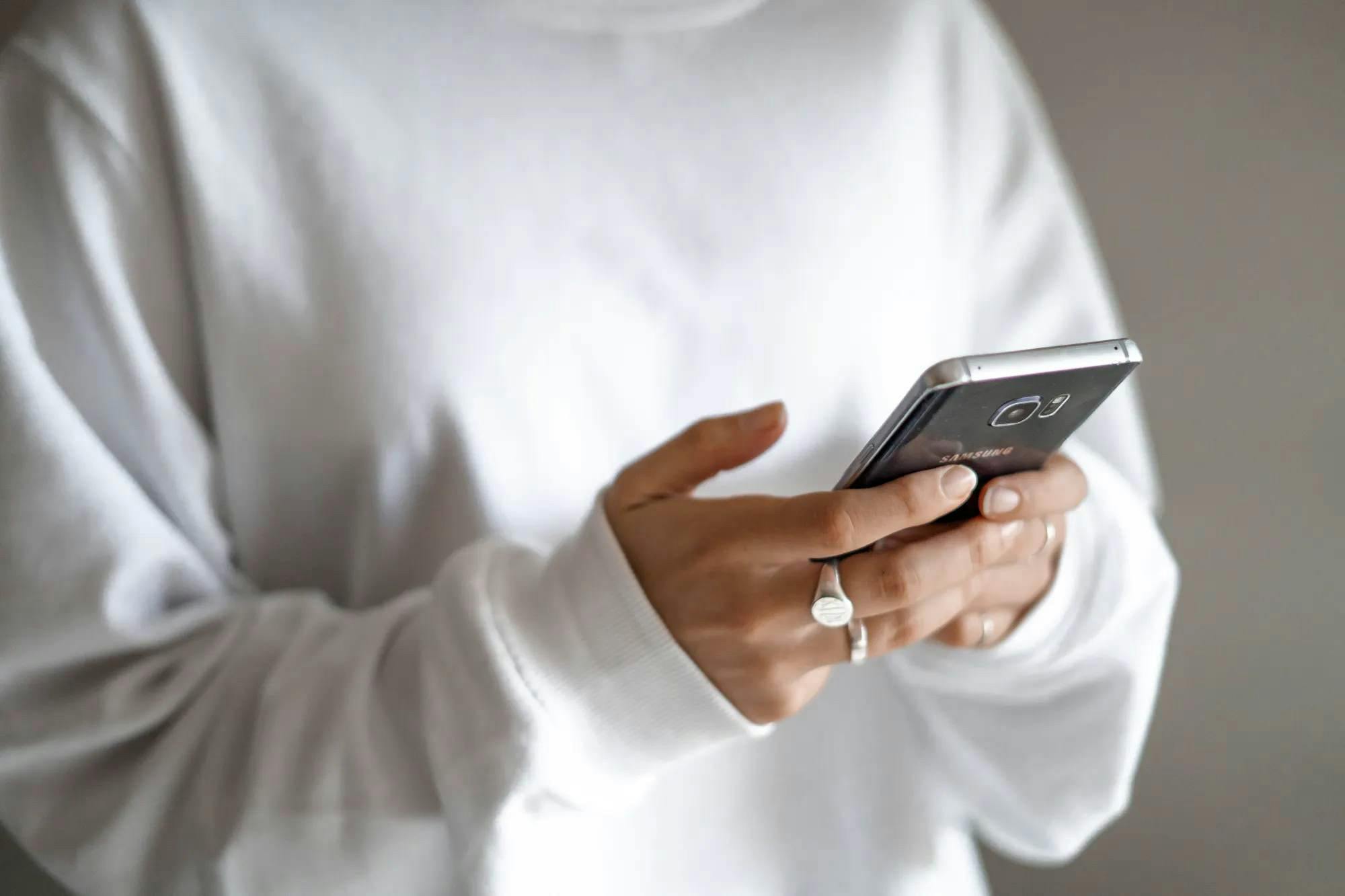 Imagem de uma mulher com um moletom branco segurando um smartphone com as mãos