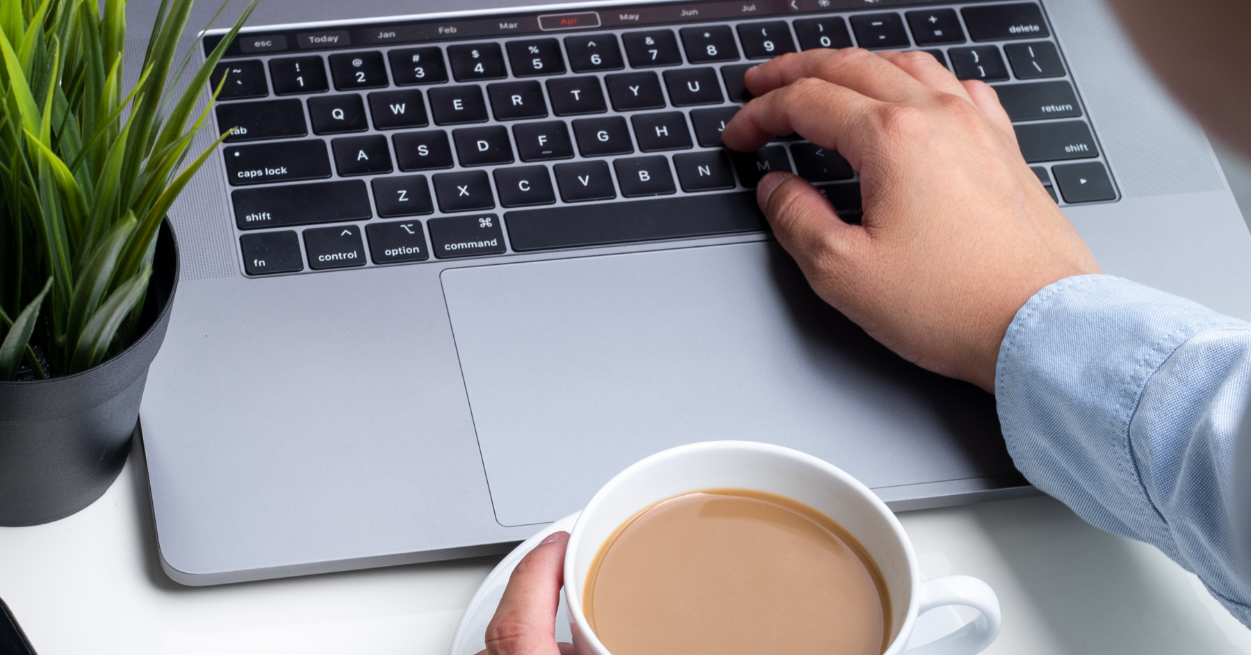 Imagem focada na mão de um homem, que digita em um laptop e segura um café com a outra mão. Foto usada para ilustrar o conteúdo sobre como abrir uma conta em casas de apostas