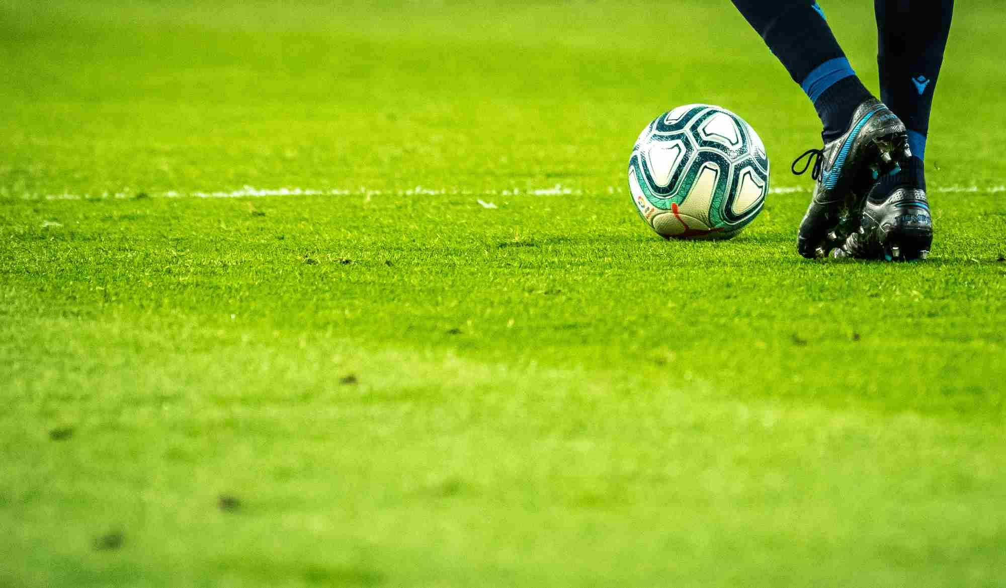 Imagem de um jogador de futebol chutando uma bola em um campo, para ilustrar a aula sobre o que são apostas esportivas