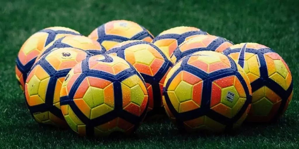 Imagem de várias bolas de futebol em um gramado. A imagem representa o conteúdo sobre o mercado acima e abaixo de gols