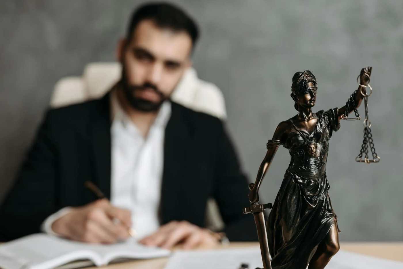 Imagem de um advogado em um escritório. No destaque da foto, vemos uma escultura com a tradicional balança do direito